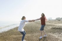 Brincalhão casal lésbico de mãos dadas e girando na praia ensolarada — Fotografia de Stock
