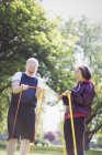 Энергичная активная старшая пара занимается спортом, используя полосы сопротивления в солнечном парке — стоковое фото