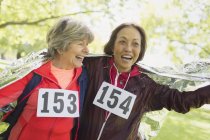 Happy active senior women finishing sports race, wrapped in thermal blanket — Stock Photo