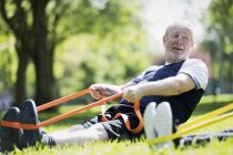 Homem idoso ativo exercitando-se no parque, alongando-se com banda de resistência — Fotografia de Stock