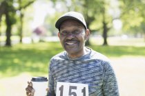 Retrato sonriente, confiado activo hombre mayor bebiendo café antes de la carrera deportiva en el parque - foto de stock