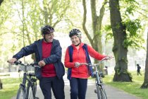 Active senior couple walking bikes in park — Stock Photo
