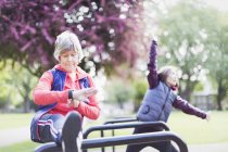 Corridore femminile anziano attivo che allunga la gamba e controlla smart watch — Foto stock