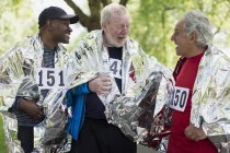 Active senior men friends finishing sports race, wrapped in thermal blankets — Stock Photo