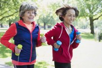 Active senior women friends jogging with hand weights in park — Stock Photo