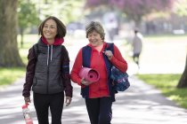 Active senior women friends with yoga mat walking in park — Stock Photo