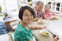 Portrait femme souriante manger des nouilles avec la famille à la table — Photo de stock