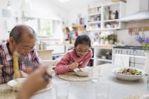 Großvater und Enkelin essen Nudeln mit Stäbchen am Tisch — Stockfoto