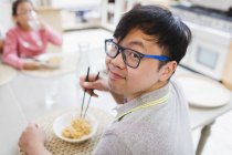 Portrait homme souriant mangeant des nouilles avec des baguettes à table — Photo de stock