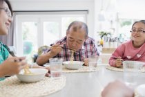 Familia multi-generación comiendo fideos con palillos en la mesa - foto de stock
