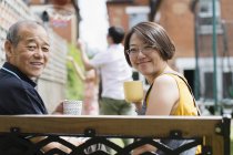 Портрет улыбающейся дочери и старшего отца, пьющих чай на скамейке во дворе — стоковое фото