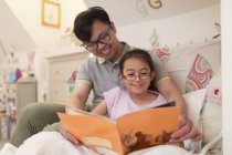 Батько і дочка читають книгу в спальні — стокове фото