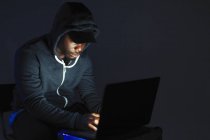 Teenage boy in hoody leaning over laptop — Stock Photo