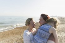 Pareja de lesbianas abrazando a su hija en la playa soleada - foto de stock