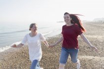 Brincalhão casal lésbico correndo na praia ensolarada — Fotografia de Stock