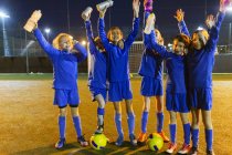 Equipe de futebol meninas confiantes retrato com garrafas de água torcendo no campo à noite — Fotografia de Stock