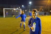 Porträt lächelnde Fußballerin, die nachts Wasser auf dem Feld trinkt — Stockfoto