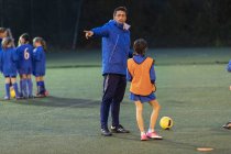 Soccer coach guiding girl soccer players practicing on field at night — Stock Photo