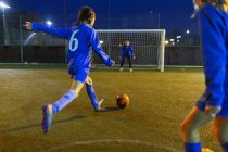 Menina jogador de futebol chutando bola em direção ao gol — Fotografia de Stock