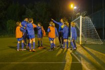 Дівчата футбольної команди слухають тренери на полі вночі — стокове фото