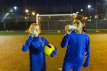 Girl soccer players taking a break, drinking water on field at night — Stock Photo