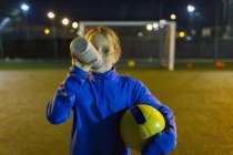 Jogadora de futebol fazendo uma pausa, bebendo água no campo à noite — Fotografia de Stock