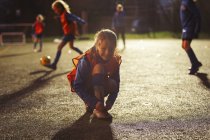 Retrato chica sonriente futbolista atando zapato en el campo por la noche - foto de stock