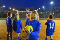Portrait smiling, enthusiastic girl enjoying soccer practice on field at night — Stock Photo
