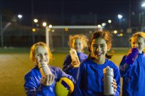 Ritratto sorridente squadra di calcio femminile in pausa dalla pratica, acqua potabile sul campo di notte — Foto stock