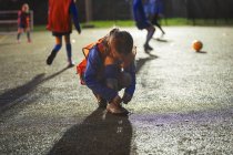 Menina jogador de futebol amarrando sapato no campo à noite — Fotografia de Stock