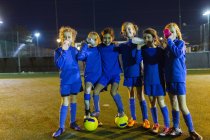 Retrato seguro de las niñas equipo de fútbol beber agua en el campo por la noche - foto de stock