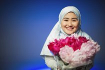 Portrait jeune femme souriante et confiante en hijab tenant des pivoines roses — Photo de stock