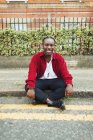 Ritratto sorridente, fiducioso ragazzo adolescente seduto sul marciapiede urbano — Foto stock