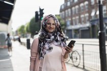 Portrait smiling, confident woman with smart phone wearing floral hijab on urban sidewalk — Stock Photo