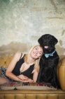 Портрет усміхненої, безтурботної молодої жінки з чорним собакою, що носить краватку на дивані — стокове фото