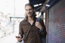 Portrait confident hipster man with smart phone on urban sidewalk — Stock Photo