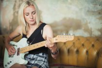 Young woman playing electric guitar on sofa — Stock Photo
