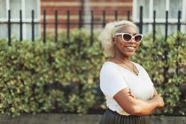 Ritratto sorridente, giovane donna sicura di sé in occhiali da sole sul marciapiede urbano — Foto stock