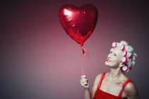 Portrait smiling senior woman with hair in curlers holding heart-shape balloon — Stock Photo