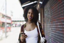 Портрет улыбающейся, уверенной молодой женщины со смартфоном на городском тротуаре — стоковое фото