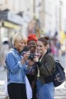 Young women friends using digital camera on urban street — Stock Photo