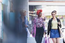 Mujeres jóvenes amigas caminando con bolsas de compras en la acera urbana - foto de stock