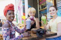 Portrait smiling young women friends drinking smoothies at sidewalk cafe — Stock Photo