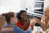 Happy young women friends toasting cocktails in apartment kitchen — Stock Photo