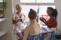 Junge Freundinnen trinken Kaffee und unterhalten sich im Wohnungsfenster — Stockfoto