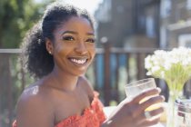 Портрет улыбающейся, уверенной молодой женщины, пьющей апельсиновый сок на солнечном балконе — стоковое фото