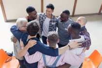 Hombres abrazándose en círculo en terapia de grupo - foto de stock