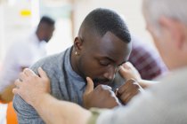 Мужчина утешает молодого человека в групповой терапии — стоковое фото