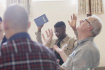 Hombres con la Biblia orando con los brazos levantados en grupo de oración - foto de stock