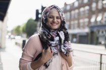 Portrait smiling, young woman wearing floral hijab on urban sidewalk — Stock Photo
